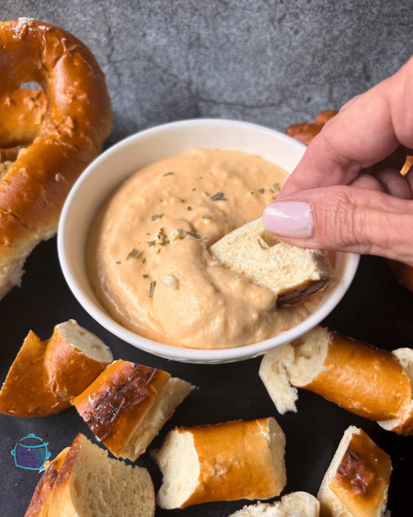Slow cooker cheese and beer dip in a bowl with a soft pretzel being dipped