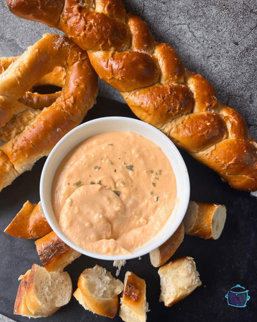 slow cooker cheese dip in a bowl surrounded by soft pretzels