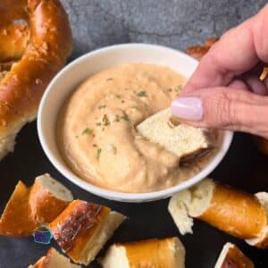 Slow cooker cheese and beer dip in a bowl with a soft pretzel being dipped