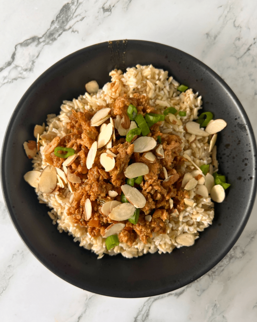 slow cooker ground Asian chicken on a bed of rice topped with sliced almonds