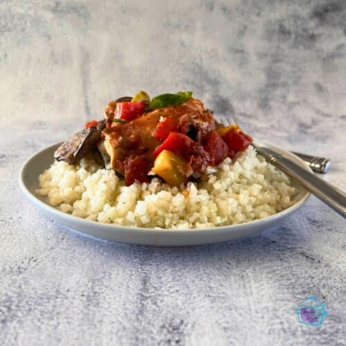 side view of a slow cooker round white bowl filled with chicken and veggie in a red sauce with some on a fork