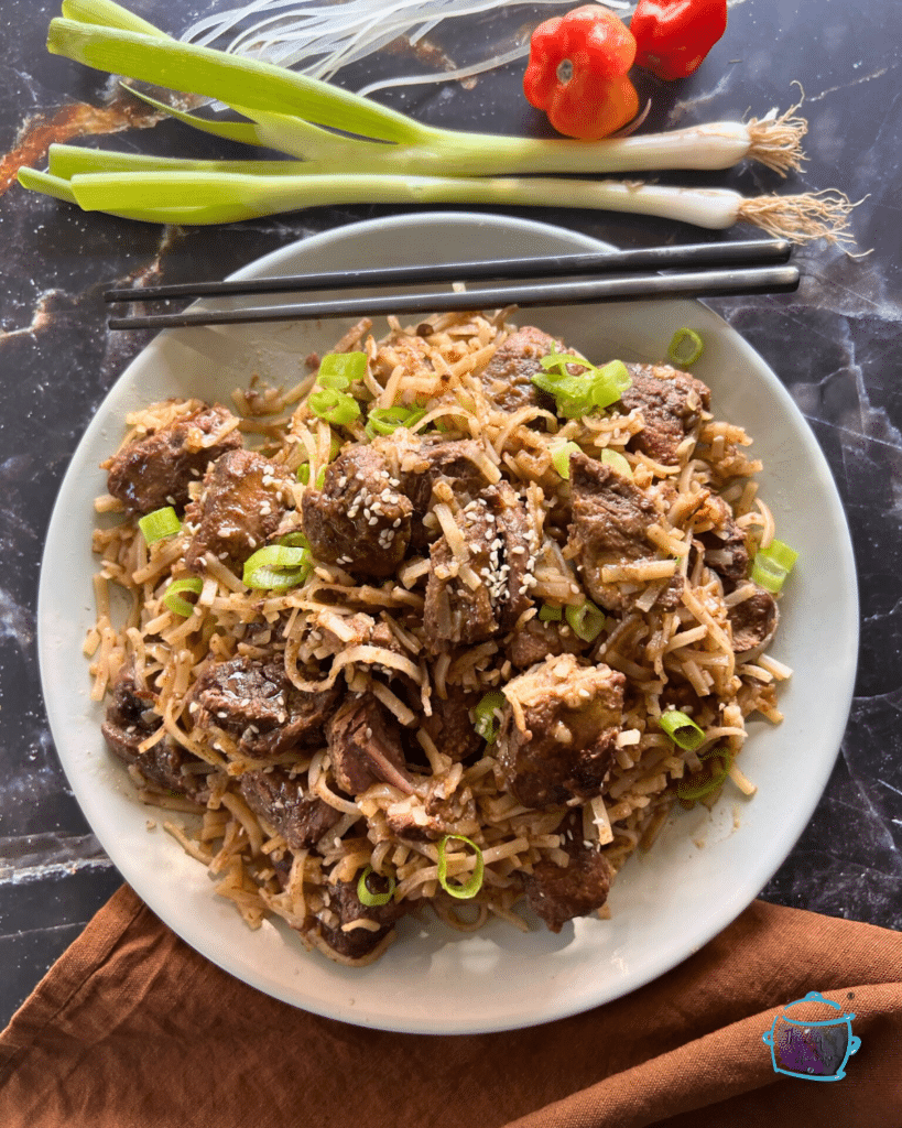 slow cooker beef with rice noodles on a white plate with black chop sticks.