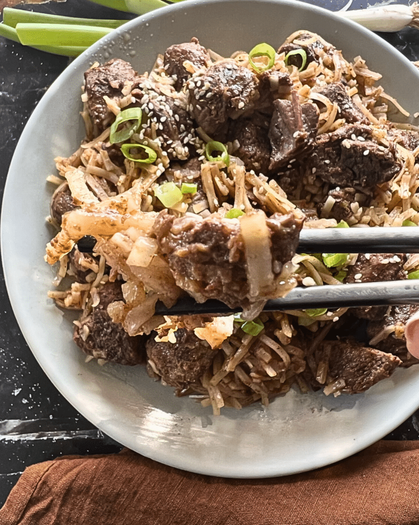 slow cooker chili lime flavored beef with rice noodles on a white plate with black chop sticks.