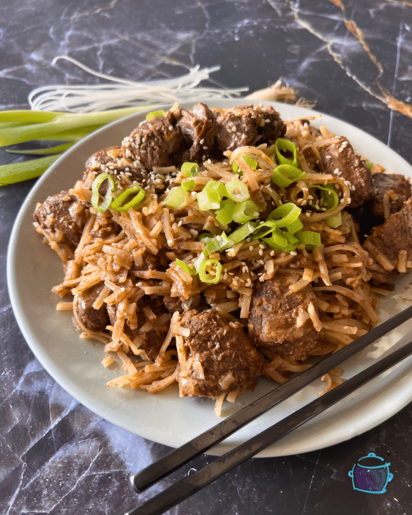 slow cooker chili lime flavored beef with rice noodles on a white plate with black chop sticks. 
