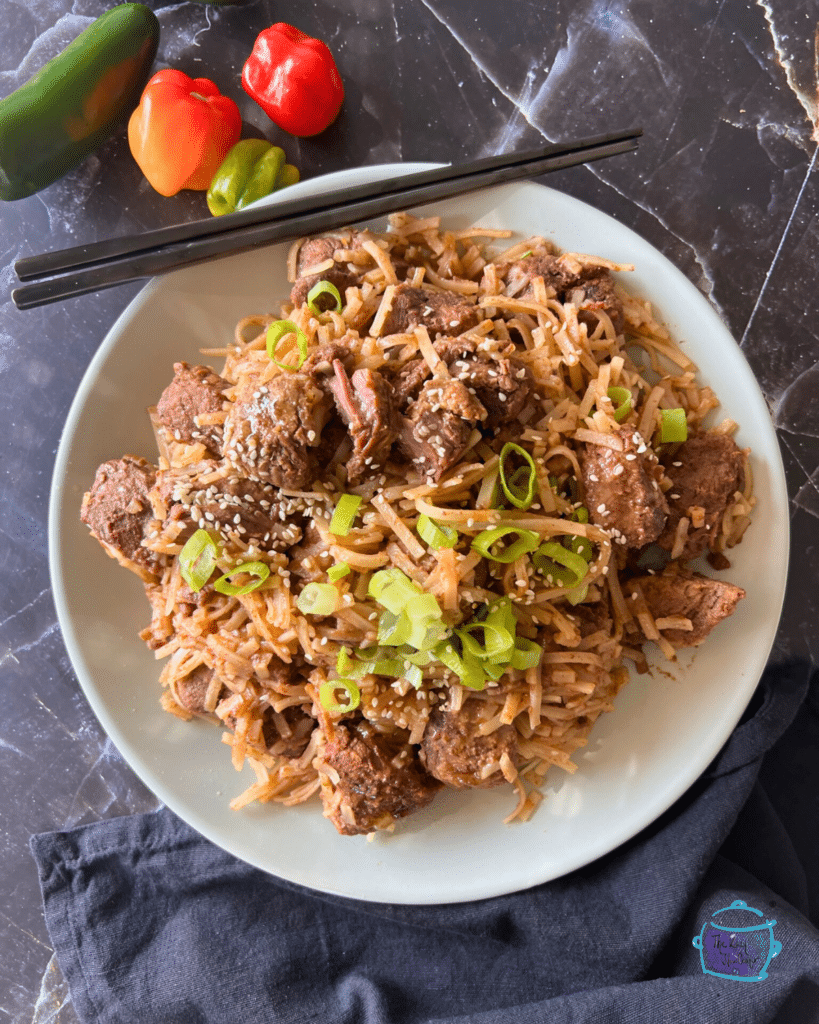 slow cooker chili lime flavored beef with rice noodles on a white plate with black chop sticks.