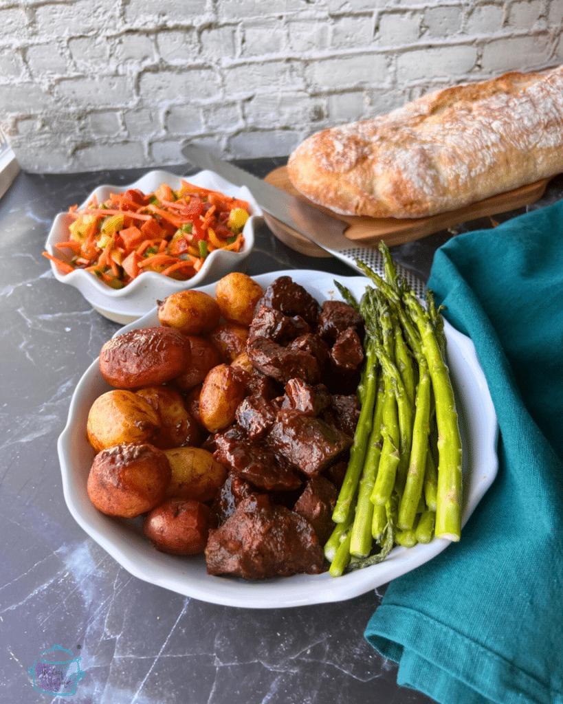 Asian steak bites on a plate with potatoes and asparagus. bread and salad are in the background