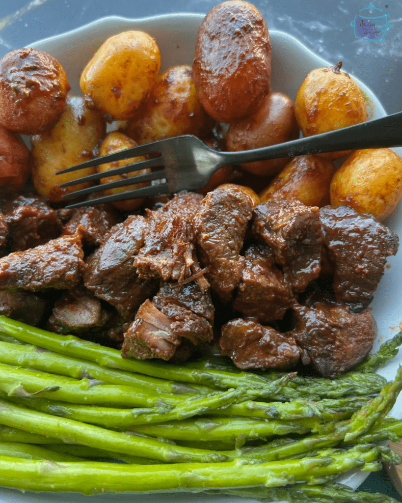 Asian steak bites on a plate with potatoes and asparagus.