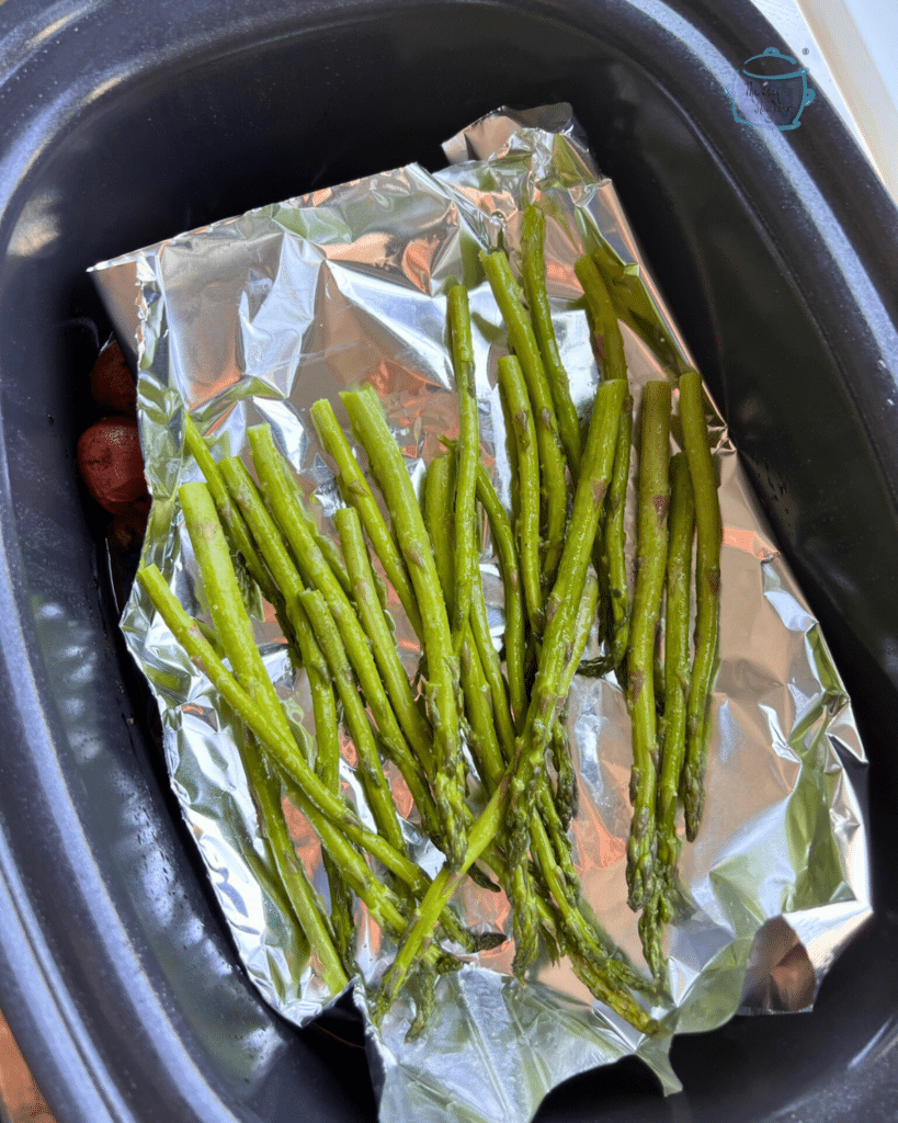 asparagus spears in a slow cooker on top of a piece of foil