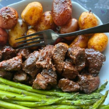 Slow cooker Asian steak bites and a fork on a plate with potatoes and asparagus.