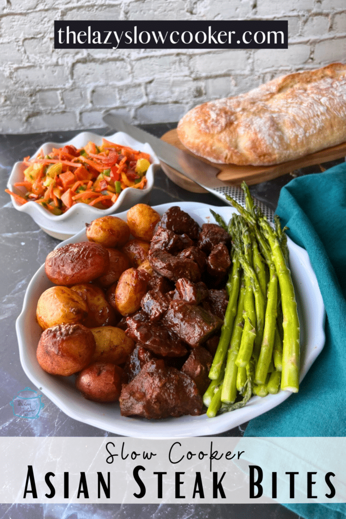 Asian steak bites on a plate with potatoes and asparagus. bread and salad are in the background