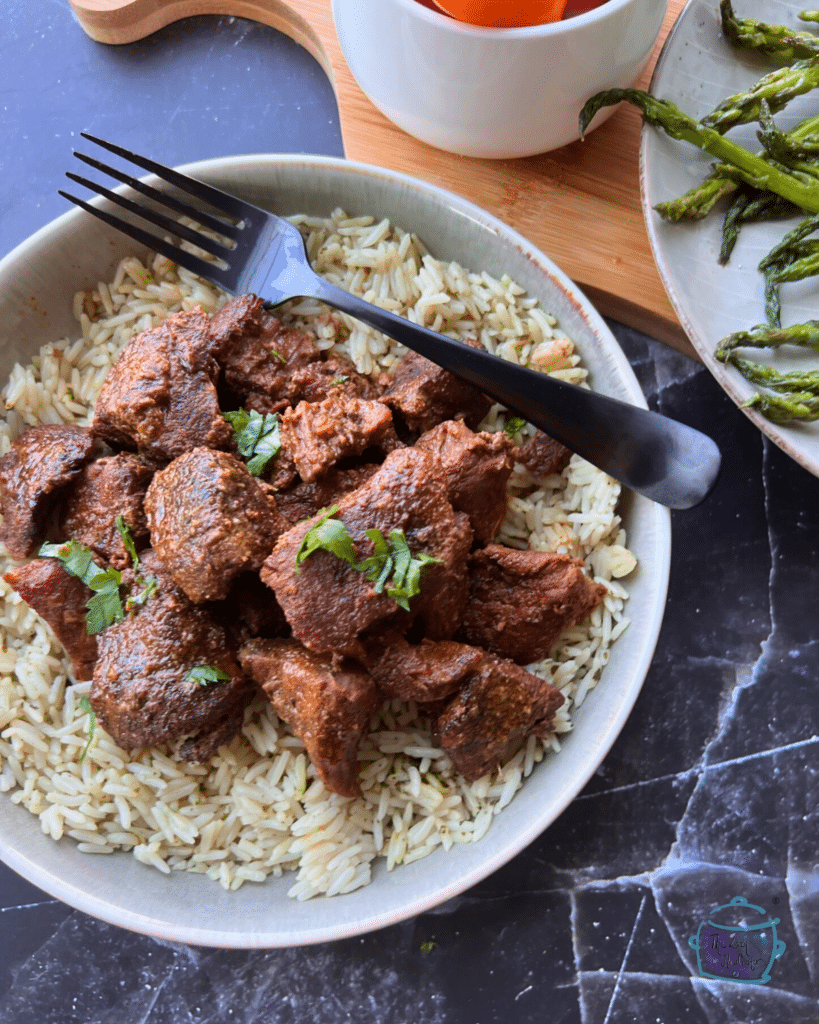 Slow cooked chunks of beef on a bed a rice with tomatoes and asparagus in the background