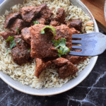 a cajun steak bite on a fork held over a plate of steak bites and rice
