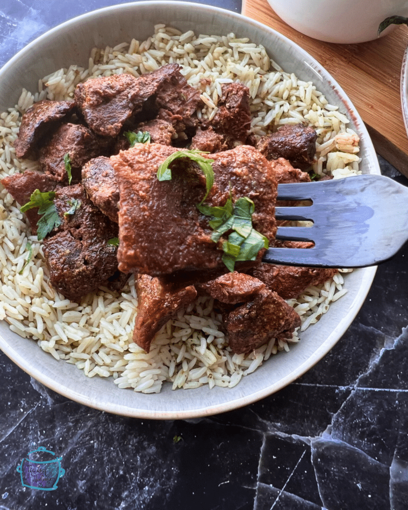 a cajun steak bite on a fork held over a plate of steak bites and rice