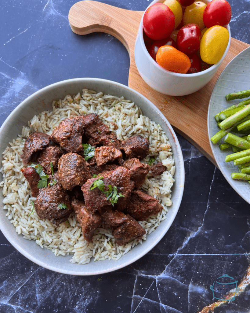 Slow cooked chunks of beef on a bed a rice with tomatoes and asparagus in the background