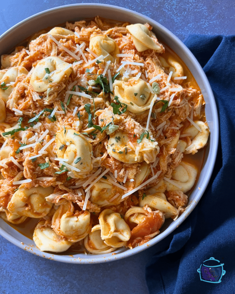 Slow cooked tortellini and shredded chicken in a red sauce in a round bowl.