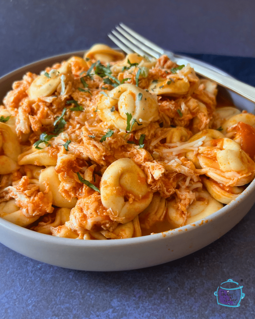 Slow cooked tortellini and shredded chicken in a red sauce in a round bowl.