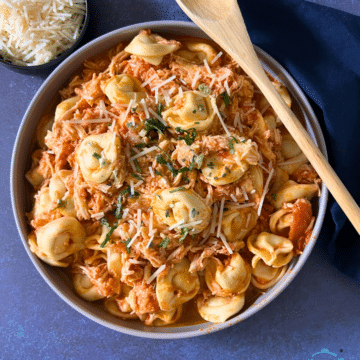 Slow cooked tortellini and shredded chicken in a red sauce in a round bowl.