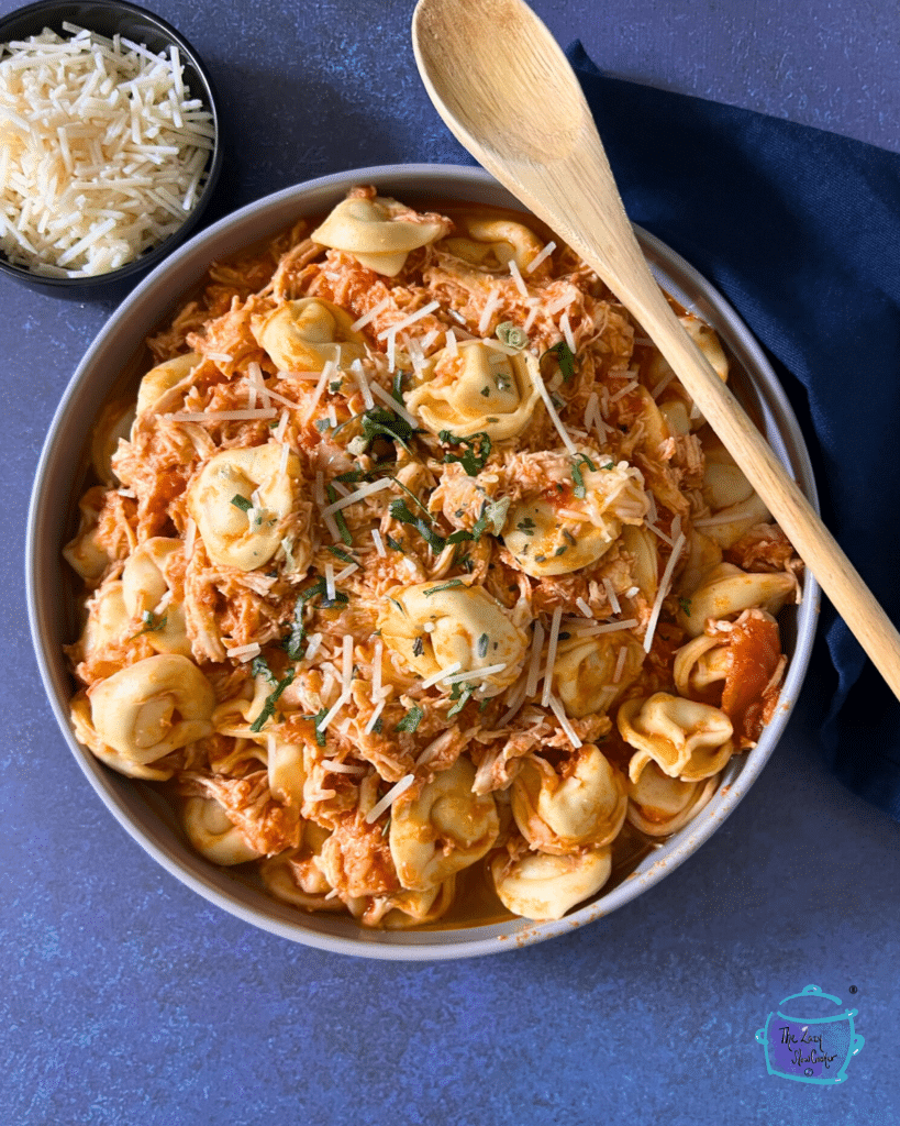 Slow cooked tortellini and shredded chicken in a red sauce in a round bowl.