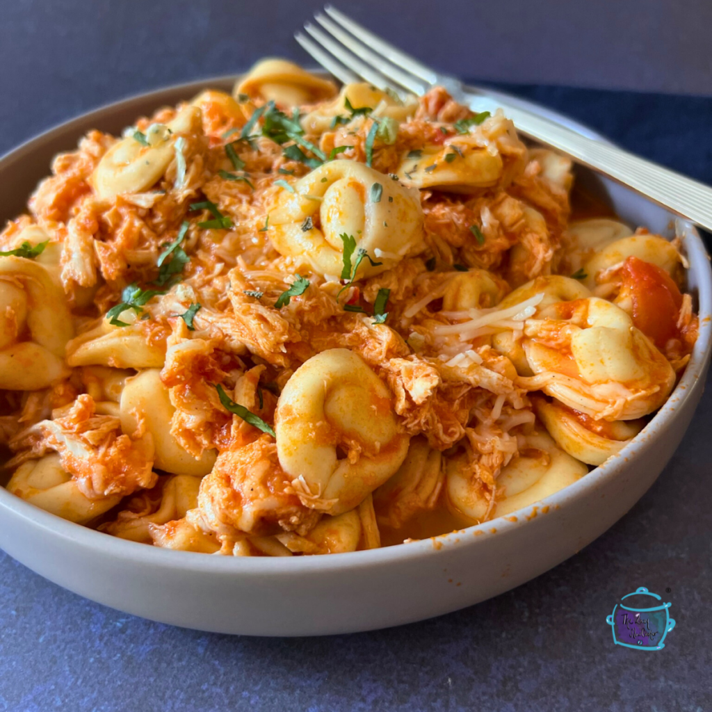 Tortellini and shredded chicken in a red sauce in a round bowl.