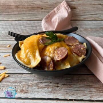 Pierogies and slices of kielbasa covered in cheese in a bowl with a fork and spoon