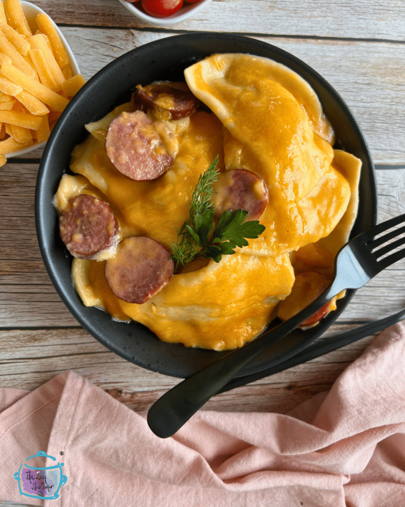 Pierogies and slices of kielbasa covered in cheese in a bowl with a fork and spoon