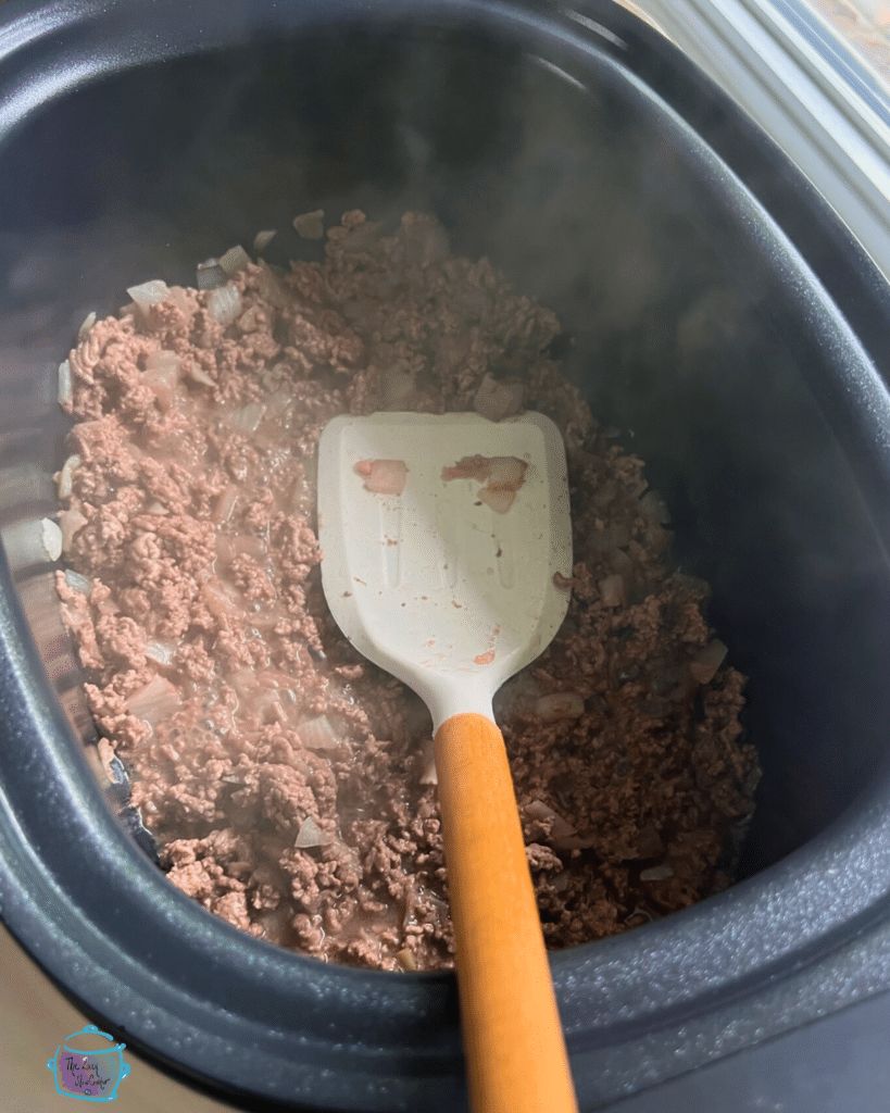 browned ground beef in a slow cooker with a browning feature and a spatula