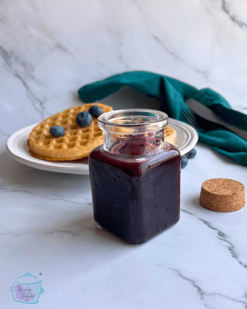 homemade blueberry sauce in jar with waffles in the background