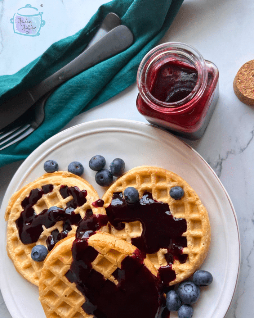 waffles topped with blueberry sauce and a jar of sauce next to them