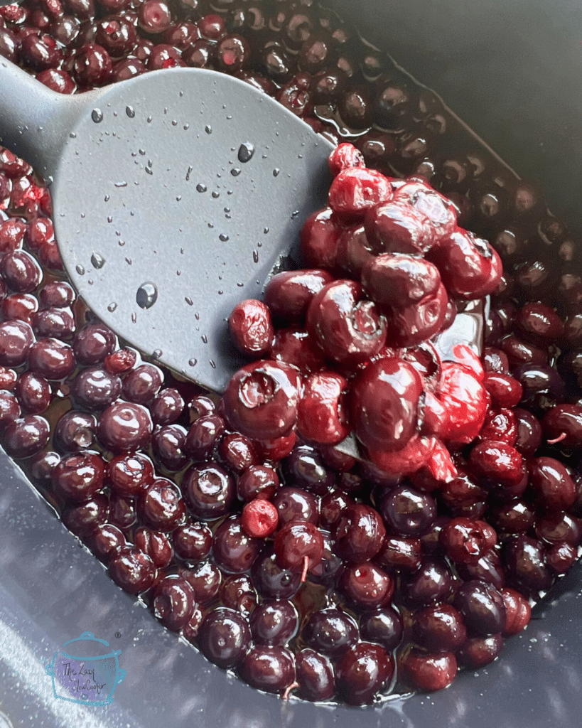 Cooked blueberries on a spoon over a slow cooker filled with the same.