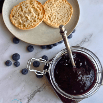 a container of thick looking blueberry butter with a knife in it and two slices of English muffin