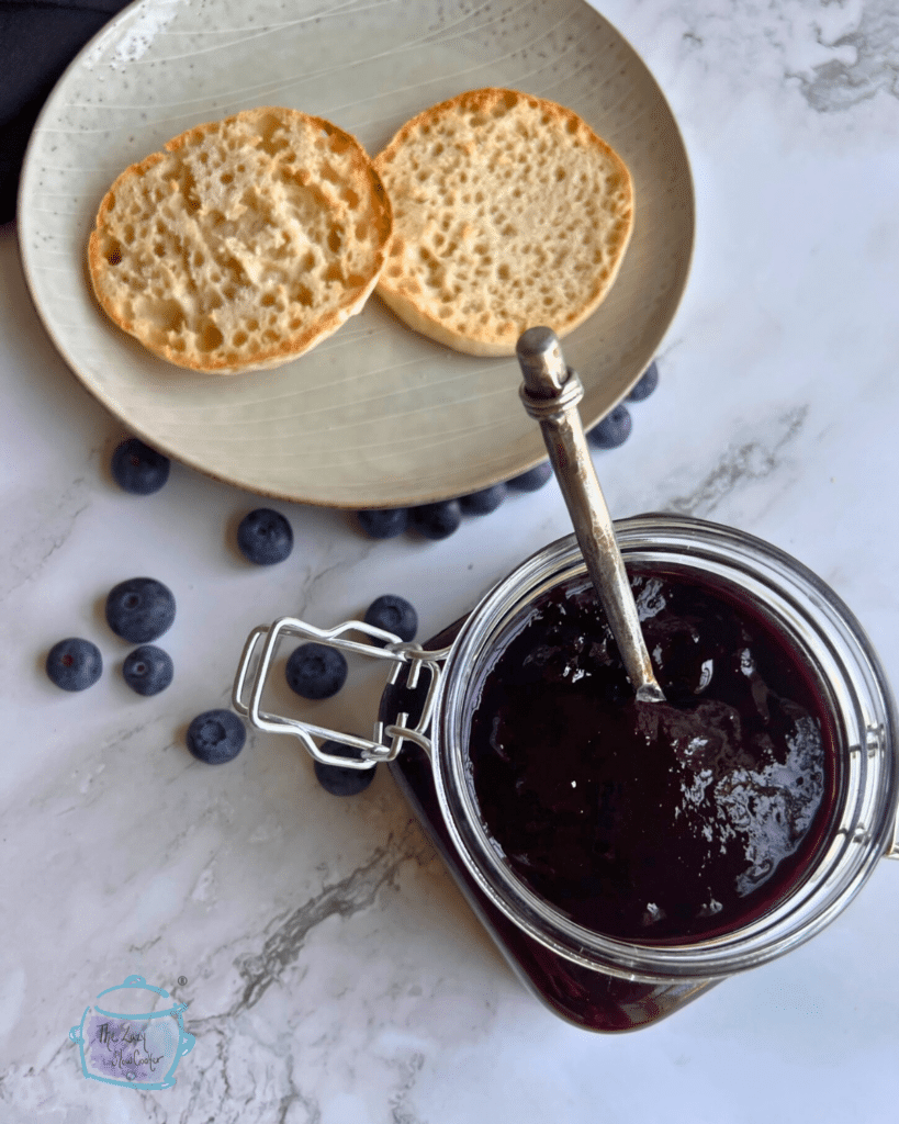 a container of thick looking blueberry butter with a knife in it and two slices of English muffin