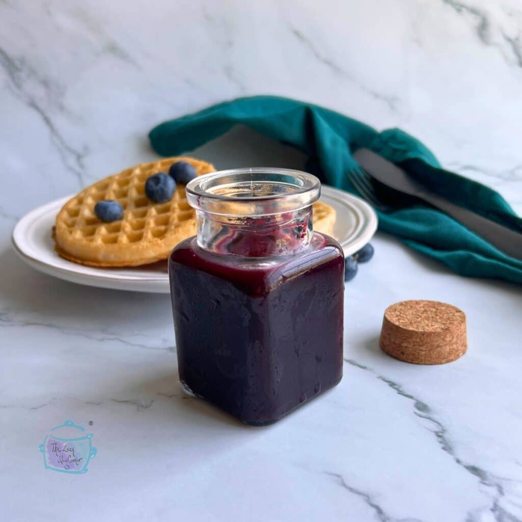 homemade blueberry sauce in jar with waffles in the background