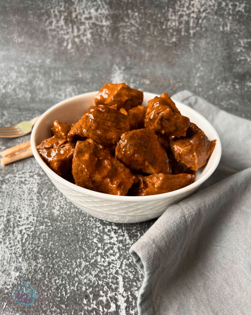 Chunks of sauce covered beef in a white bowl