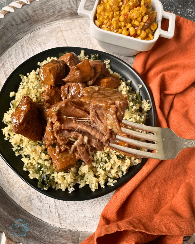 Chunks of sauce covered beef on a plate of riced cauliflower and broccoli. A fork is holding one tender looking chunk in the foreground