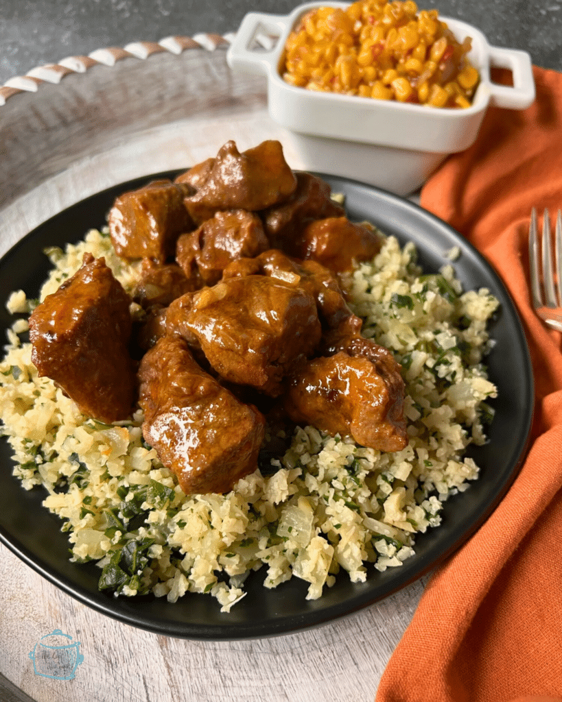 Chunks of sauce covered beef on a plate of riced cauliflower and broccoli.