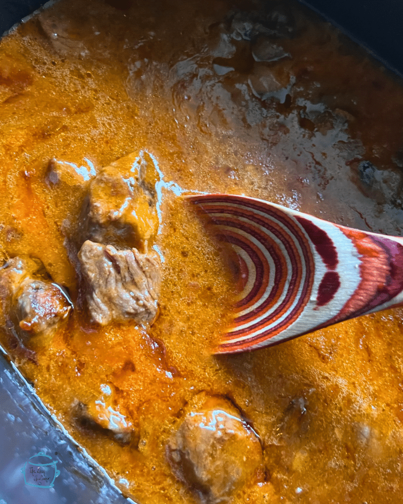 French beef tips in slow cooker with a large wooden spoon