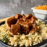 Chunks of sauce covered beef on a plate of riced cauliflower and broccoli.