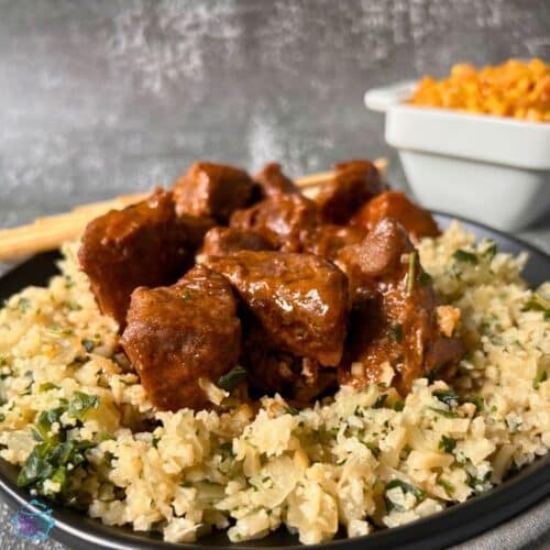 Chunks of sauce covered beef on a plate of riced cauliflower and broccoli.