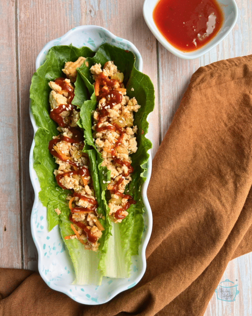 two Romaine lettuce leaves filled with a ground turkey mixture on a long plate with a napkin an dipping sauce on the side.