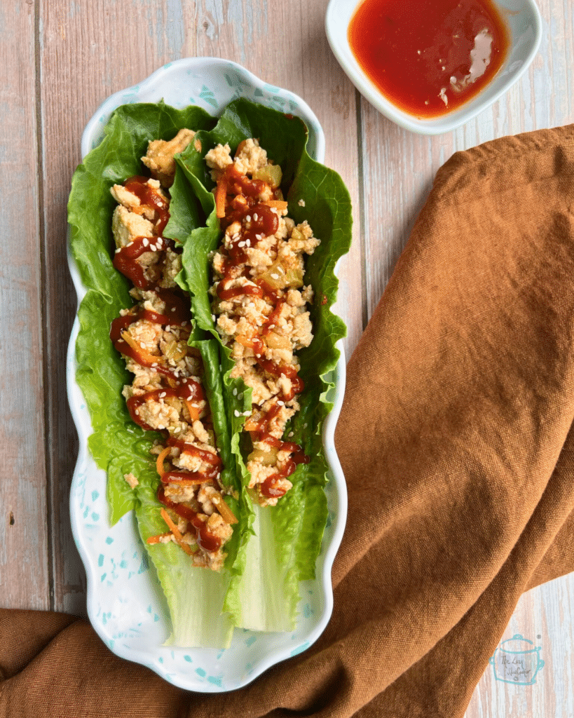 two Romaine lettuce leaves filled with sweet chili turkey lettuce wraps mixture on a long plate with a napkin an dipping sauce on the side.  