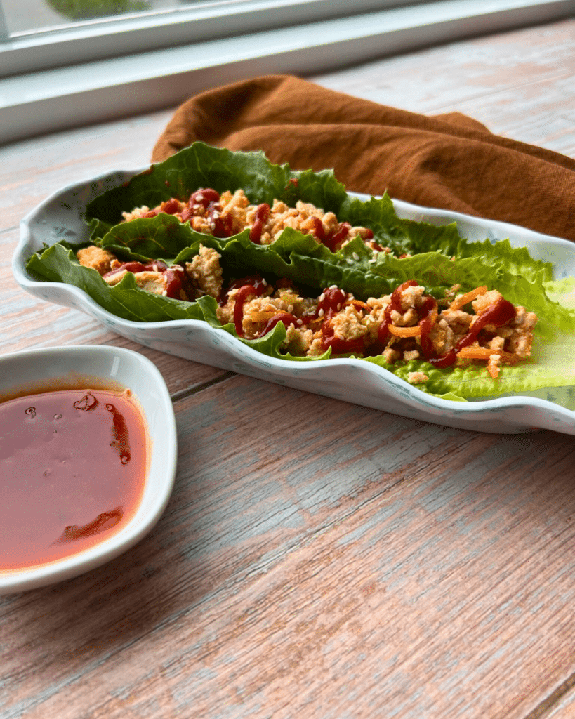 two Romaine lettuce leaves filled with the sweet chili turkey lettuce wraps mixture on a long plate with a napkin an dipping sauce on the side.