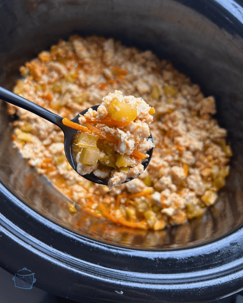 a slow cooker with a spoon in front of it holding some ground cooked ground turkey and veggies in sauce.