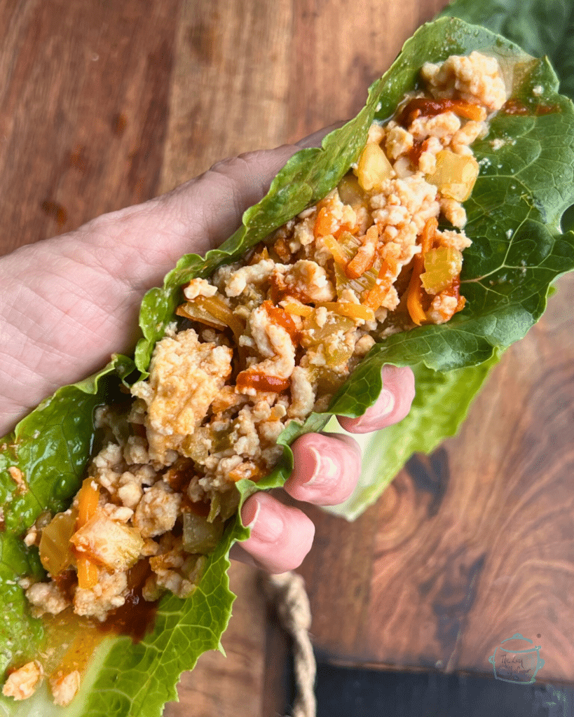 Slow cooker ground turkey in a lettuce leaf held in a hand.