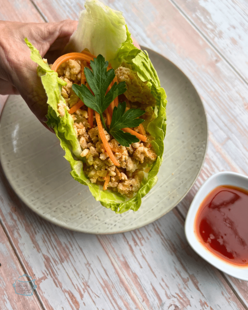 sweet chili turkey lettuce wrap being held by a hand over a plate. 