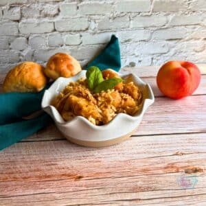peach balsamic chicken in a white bowl with a peach and some rolls