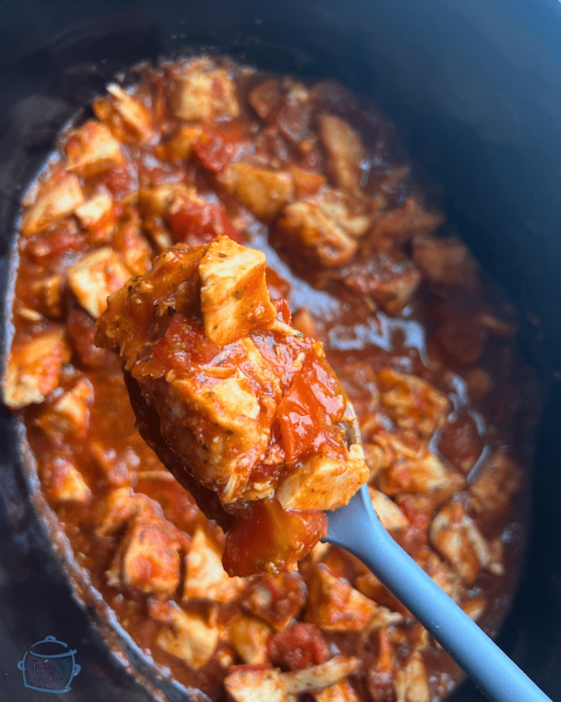 a slow cooker full of tomato balsamic chicken with a spoon