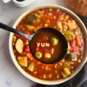 a bowl of alphabet soup with a spoonful of the same. the noodles in the spoon spell the word YUM.
