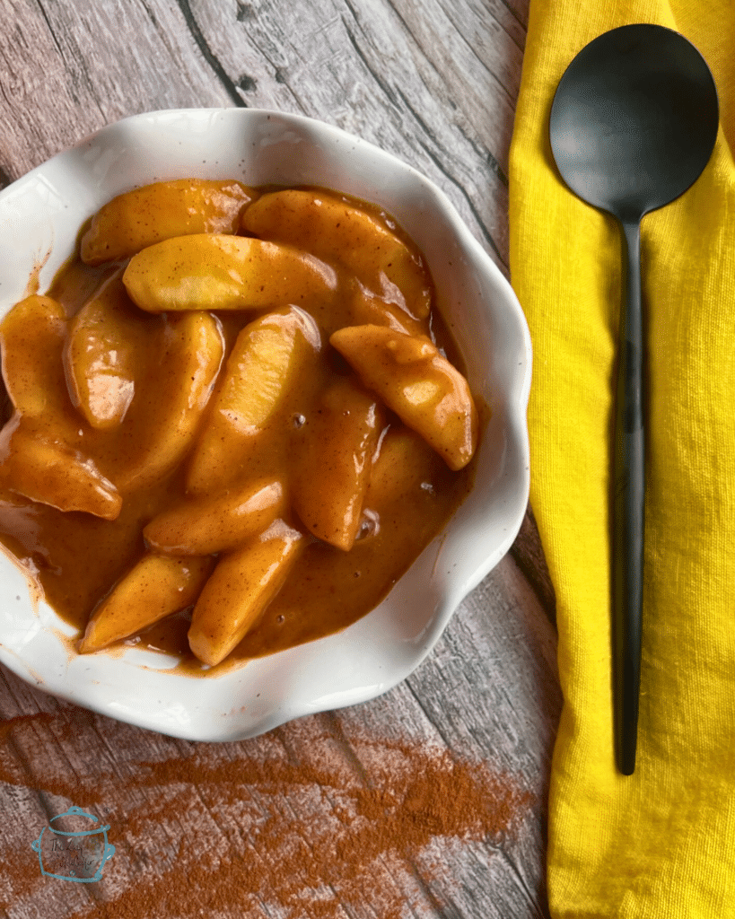 A white bowl filled with slow cooked caramel apple pie filling with a spoon on a yellow napkin