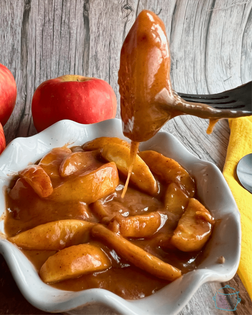 An apple slice on a fork with caramel sauce dripping off of it.