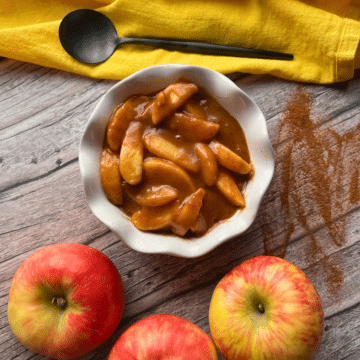 A white bowl filled with slow cooked caramel apple pie filling with a spoon on a yellow napkin